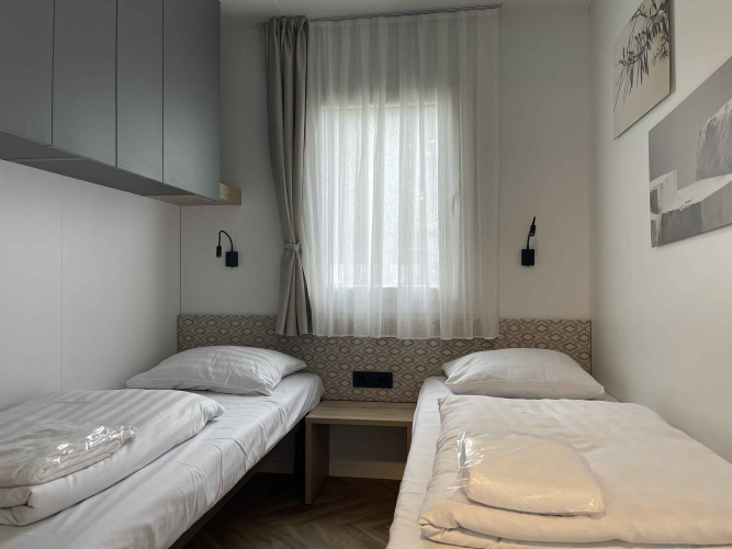 Habitación de albergue moderna con dos camas individuales, ventana y decoración minimalista en Belsano 6.