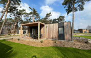 Modern Belsano 6 lodge at Zilverstrand, Belgium, with wooden exterior, terrace, and trees in the background.