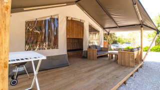 Tienda safari con terraza de madera, cómodos sofás, barbacoa y aire acondicionado para relajarse.