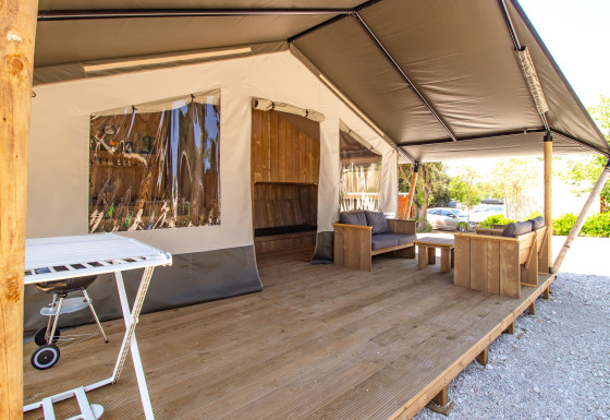 Tienda safari con terraza de madera, cómodos sofás, barbacoa y aire acondicionado para relajarse.