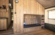 Interno di una tenda safari con pavimento in legno, panca, scaffali, finestra e angolo cucina.