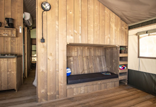 Interior of a safari tent with wooden floor, built-in bench, shelving, window and a kitchenette area.