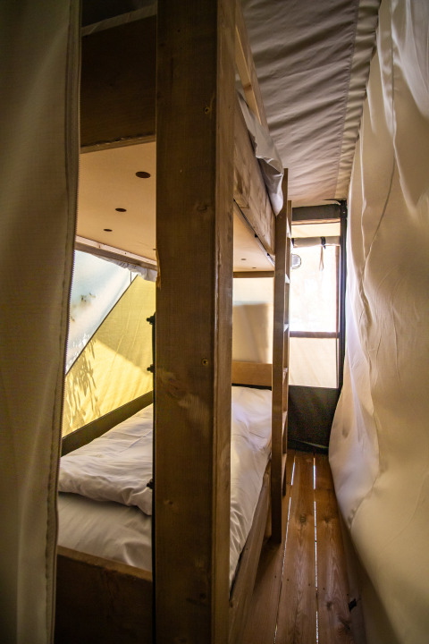 Interno di una tenda safari con letti a castello in legno, pavimento in legno e pareti di tela illuminate.