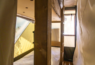 Interno di una tenda safari con letti a castello in legno, pavimento in legno e pareti di tela illuminate.