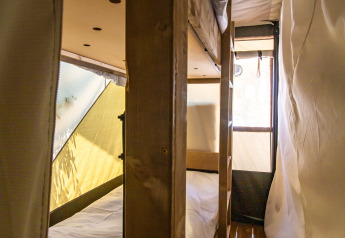 Intérieur d'une tente safari avec lits superposés en bois, sol en bois et murs en toile éclairés par la lumière.