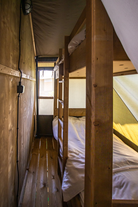 Intérieur d’une tente safari avec lits superposés en bois, plancher en bois et lumière naturelle.