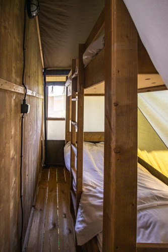 Intérieur d’une tente safari avec lits superposés en bois, plancher en bois et lumière naturelle.