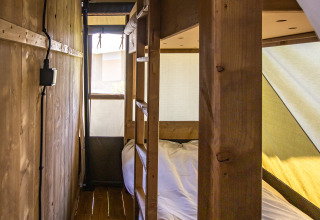 Interieur van een safaritent met houten stapelbedden, houten vloer en invallend natuurlijk licht.