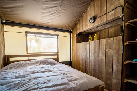 Vista interior de una tienda safari acogedora, con paredes de madera, cama doble y luz natural del exterior.