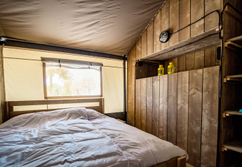 Vista interna di una tenda safari accogliente con pareti di legno, letto matrimoniale e luce naturale dalla finestra.