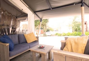 Tenda safari con servizi igienici privati e aria condizionata, area relax con cuscini colorati.