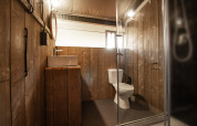 Baño en tienda safari con paredes de madera, lavabo moderno, inodoro y cabina de ducha de cristal.