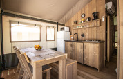 Interieur van een safaritent met moderne keuken, eettafel, sanitair en airconditioning.
