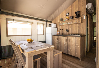 Interno di una tenda safari con cucina moderna, tavolo da pranzo, servizi igienici e aria condizionata.