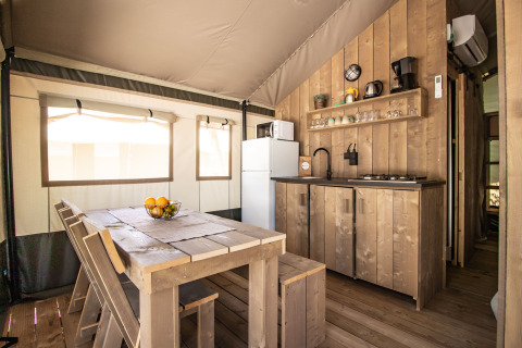 Vue intérieure d'une tente safari avec cuisine moderne, table à manger, sanitaires et climatisation.