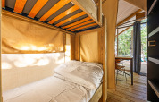 Interior view of Safari tent Bella Vista with bunk bed, wooden furniture, and scenic outdoor nature view.
