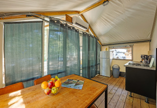 Vista interior de la tienda Safari Bella Vista con aire acondicionado, mesa de comedor y cocina en Camping Porto Sole.