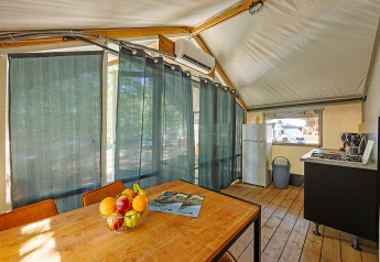 Vista interna della tenda Safari Bella Vista con aria condizionata, tavolo da pranzo e cucina al Camping Porto Sole.