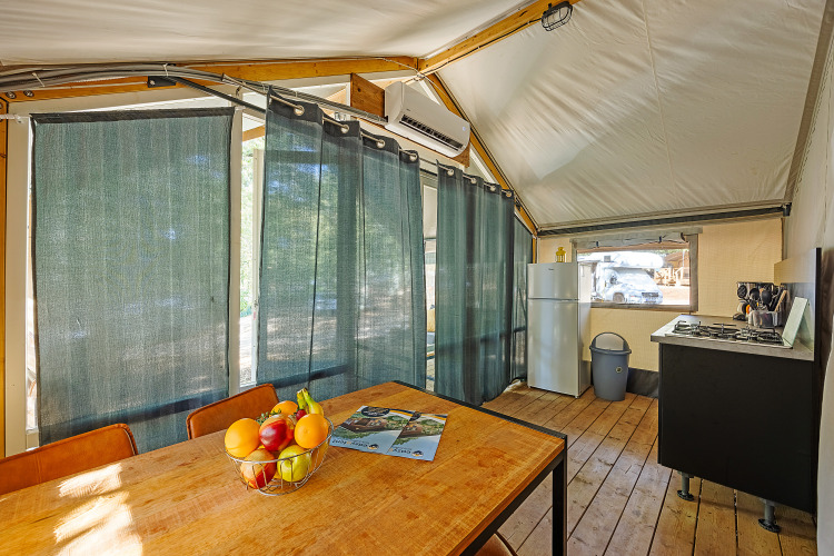 Vue intérieure de la tente Safari Bella Vista avec climatisation, table à manger et cuisine au Camping Porto Sole.