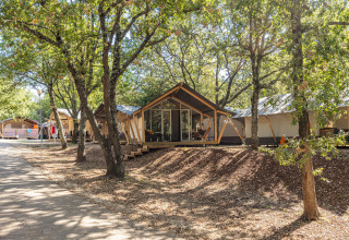 Tente safari Bella Vista avec climatisation, située dans un camping boisé entouré d’arbres verts.