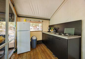 Vista interna di una cucina in tenda safari con fornello, frigorifero, pattumiera e pavimento in legno.