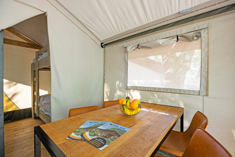 Interior view of Safari tent Bella Vista with dining table, fruit bowl, and bunk beds at Camping Porto Sole.