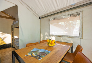 Interno della tenda Safari Bella Vista con tavolo da pranzo, ciotola di frutta e letti a castello a Camping Porto Sole.