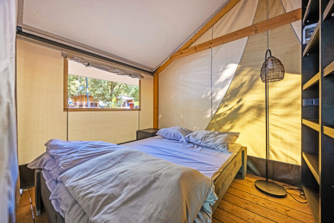 Vista interna della tenda Safari Bella Vista con aria condizionata, letto e pavimento in legno illuminato.