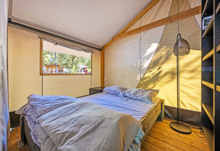 Vista interna della tenda Safari Bella Vista con aria condizionata, letto e pavimento in legno illuminato.
