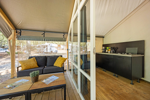 Safari tent Bella Vista with air conditioning, stylish sofa, kitchen, and view of outdoors from deck.