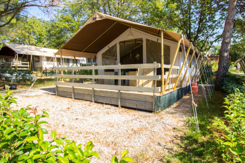 Tienda safari con porche, instalaciones sanitarias y aire acondicionado, rodeada de árboles verdes.