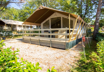 Safari-telt med terrasse, sanitære faciliteter og aircondition, omgivet af grønne træer og buske.