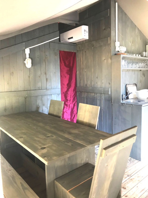 Interior de una tienda safari en Camping Valkanela, Croacia, con mesa y sillas de madera y aire acondicionado.