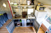 Pequeña cocina en una tienda safari con estanterías abiertas, fogón, nevera, microondas y utensilios.