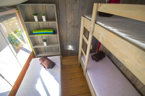 Interior view of a safari tent with bunk beds, shelving, and rolled towels at Camping Valkanela, Croatia.