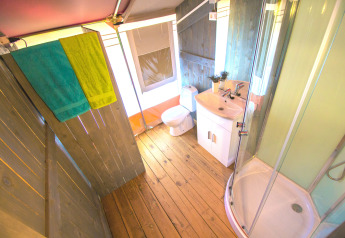 Bagno in tenda safari con pavimento in legno, doccia, wc, lavabo e asciugamani colorati a Camping Valkanela.