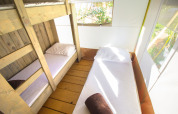 Vista interna di una tenda safari con letto a castello, letto singolo, lenzuola bianche e luce naturale.