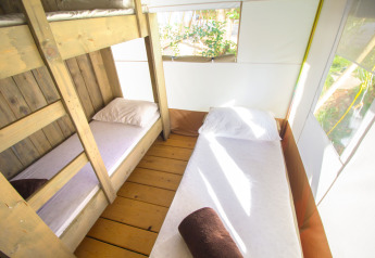 Vista interna di una tenda safari con letto a castello, letto singolo, lenzuola bianche e luce naturale.