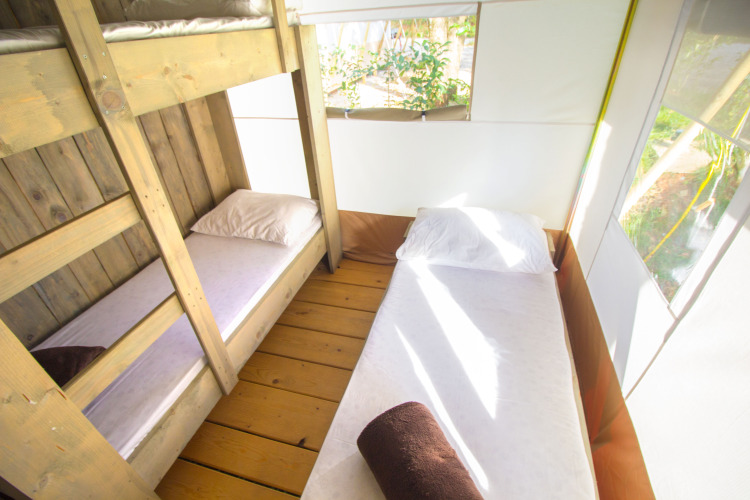 Interieur van een safaritent met stapelbed, eenpersoonsbed, witte lakens en veel daglicht.