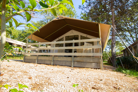 Safari tent with covered wooden porch in a scenic, tree-filled area on a sunny day, seen from below.