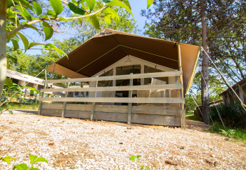 Safari tent with covered wooden porch in a scenic, tree-filled area on a sunny day, seen from below.