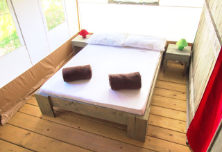 Habitación de tienda safari con cama doble, suelos de madera y luz natural entrando por las ventanas.