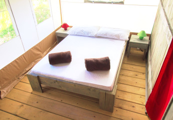 Camera da letto in una tenda safari con letto matrimoniale, pavimento in legno e comodini.