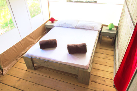 Knusse slaapkamer in een safaritent met tweepersoonsbed, houten vloer en nachtkastjes.