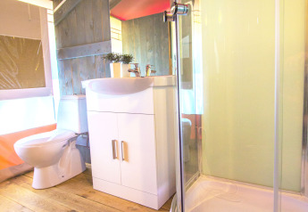 Bagno in una tenda safari con pavimento in legno, box doccia, WC e mobile lavabo bianco.