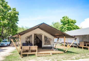 Suite de tente safari moderne avec terrasse ombragée, salon extérieur et arbres verdoyants aux alentours.
