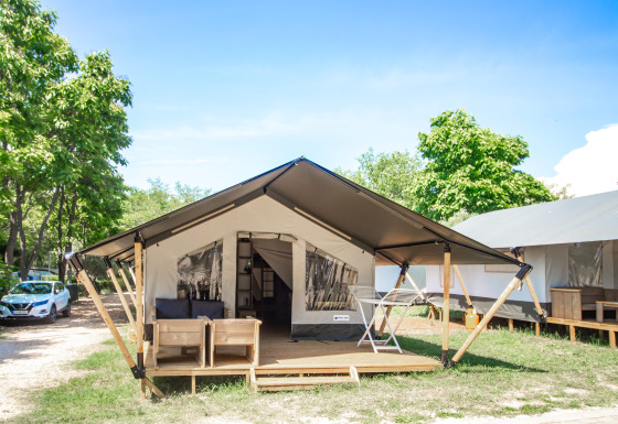 Suite de tente safari moderne avec terrasse ombragée, salon extérieur et arbres verdoyants aux alentours.