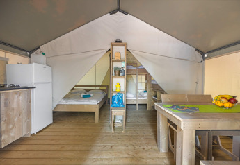 Interno di una tenda safari con pavimento in legno, letti, tavolo da pranzo, frigorifero e cucina.