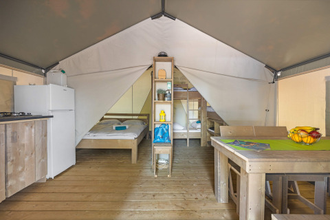 Interior of a safari tent featuring wooden floors, beds, dining table, refrigerator, and kitchen area.
