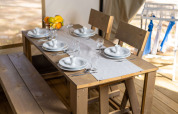 Tavolo apparecchiato in una tenda safari, con panche e sedie in legno, piatti bianchi e frutta fresca.